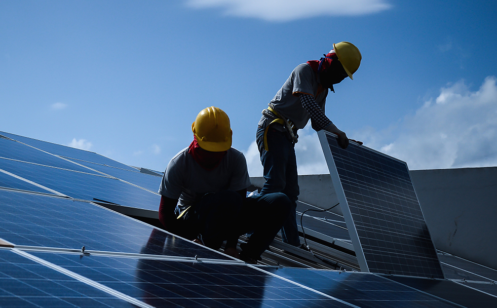 Men in hardhats installing solar panels on a roof