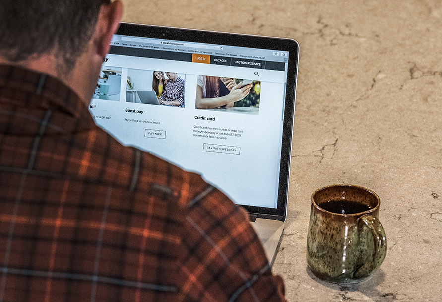 Man in flannel shirt looking at Black Hills Energy website on laptop.