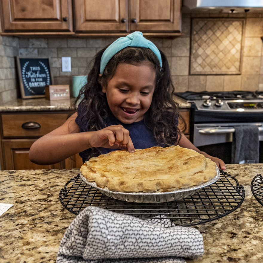 Little girl in the kitchen poking at a pie