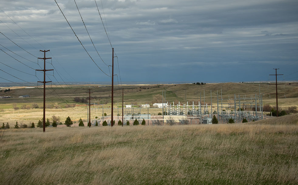 Electric transmission lines going into substation on the prairie under a cloudy sky.