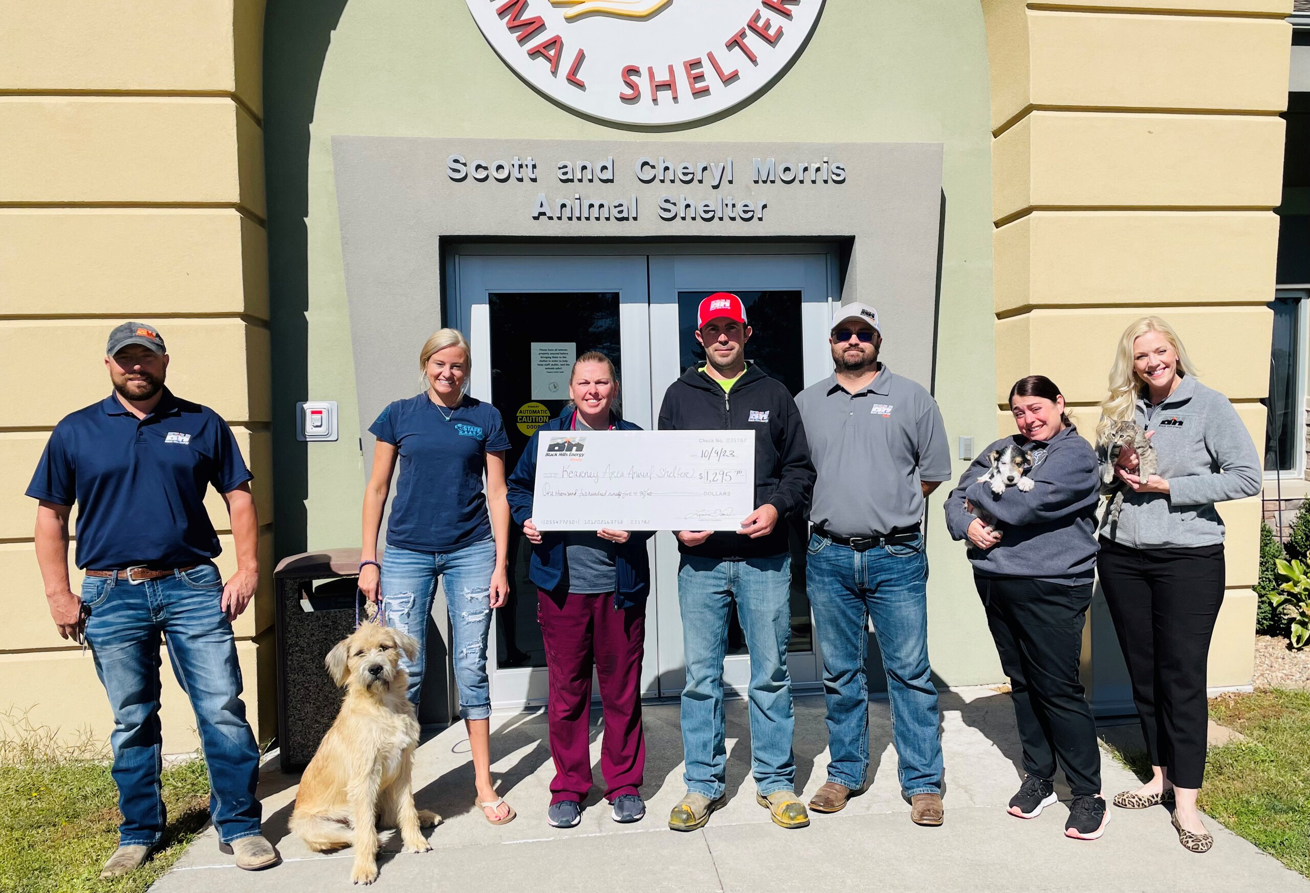 group of people doing a check presentation in front of animal shelter while holding dogs