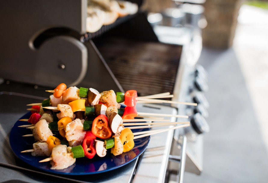 Plate of skewered vegetables on a plate sitting next to a grill outside