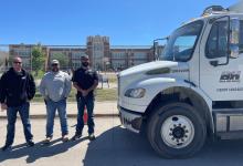 men standing by work truck outside school