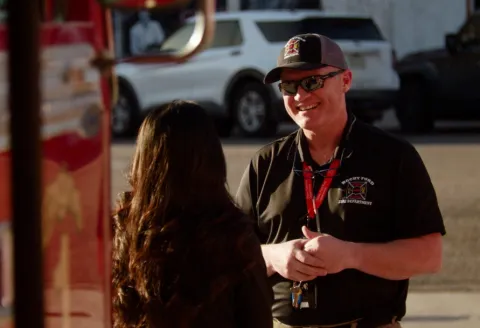 A firefighter speaking to a woman next to a firetruck