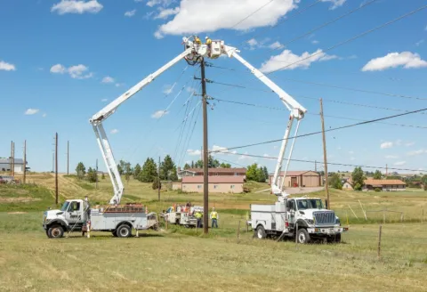 Two bucket trucks working on a power pole in a residential area